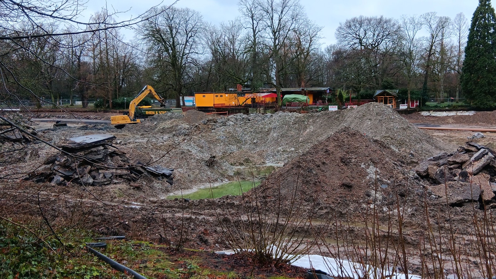 Ein Bagger steht auf dem Grund des Volksgartenweihers inmitten größerer Schlammberge.