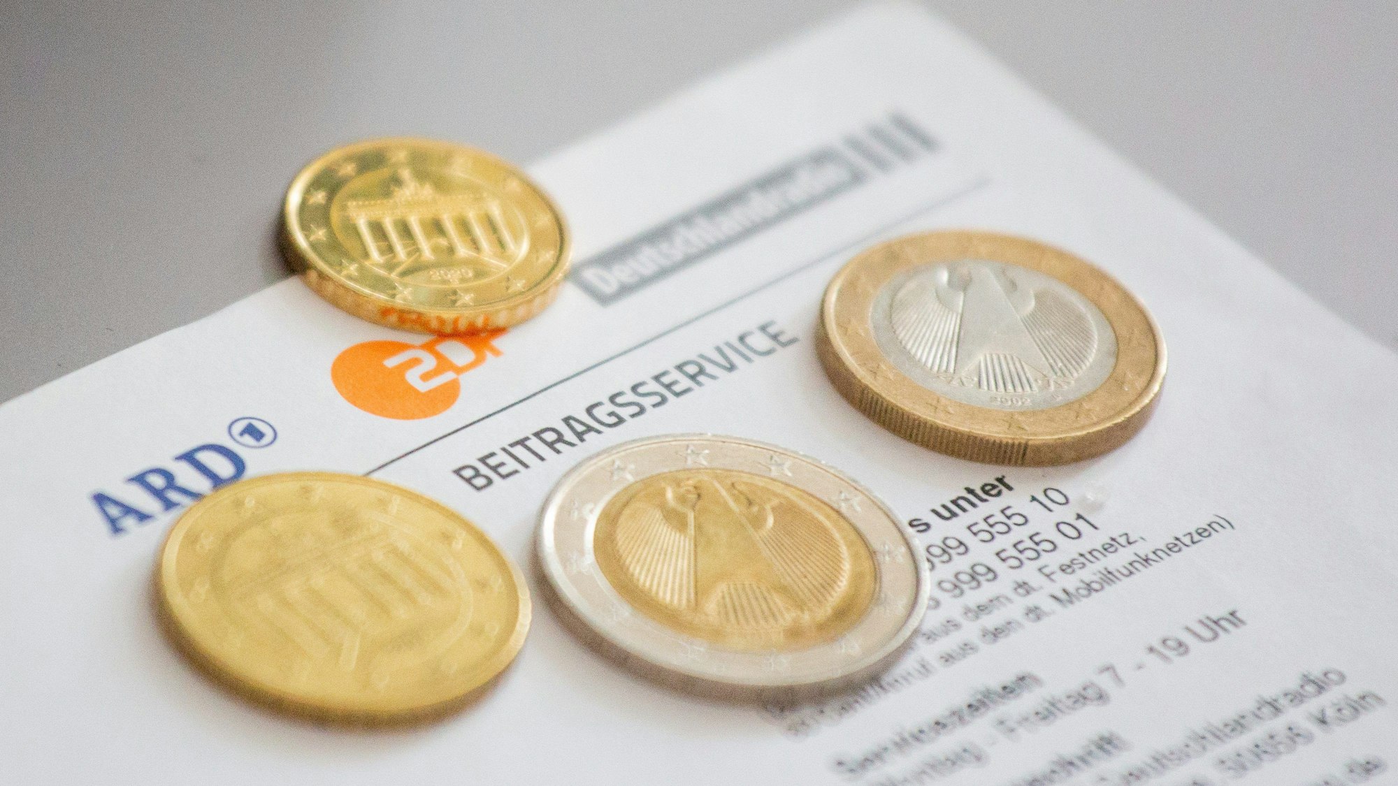 Euromünzen liegen auf einem Anschreiben zur Anmeldung für die Rundfunkgebühren, neben den Logo von ARD, ZDF und Deutschlandfunk.