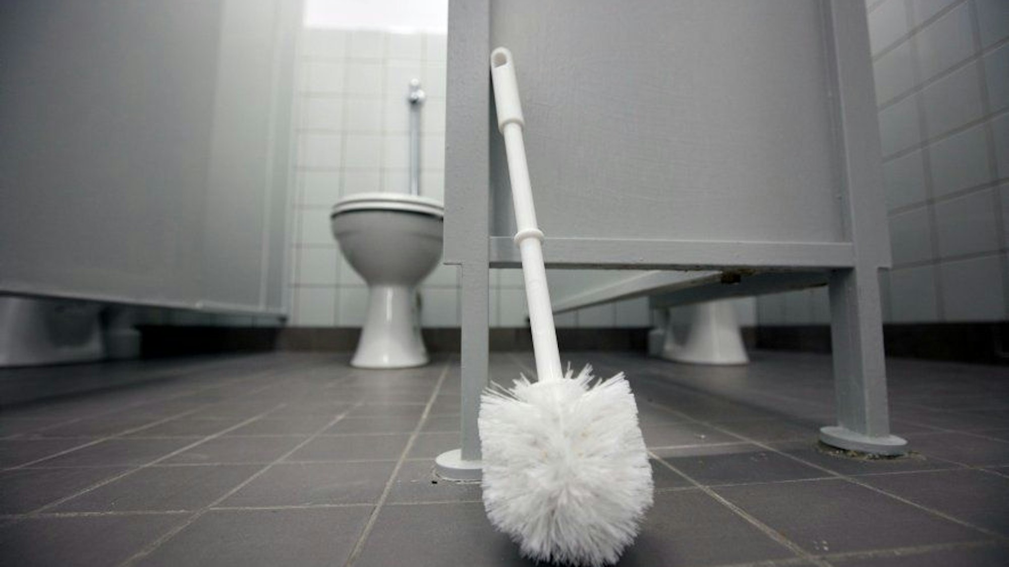 Eine Klobürste lehnt an einer Tür in einem frisch renovierten Toilettentrakt einer Schule.