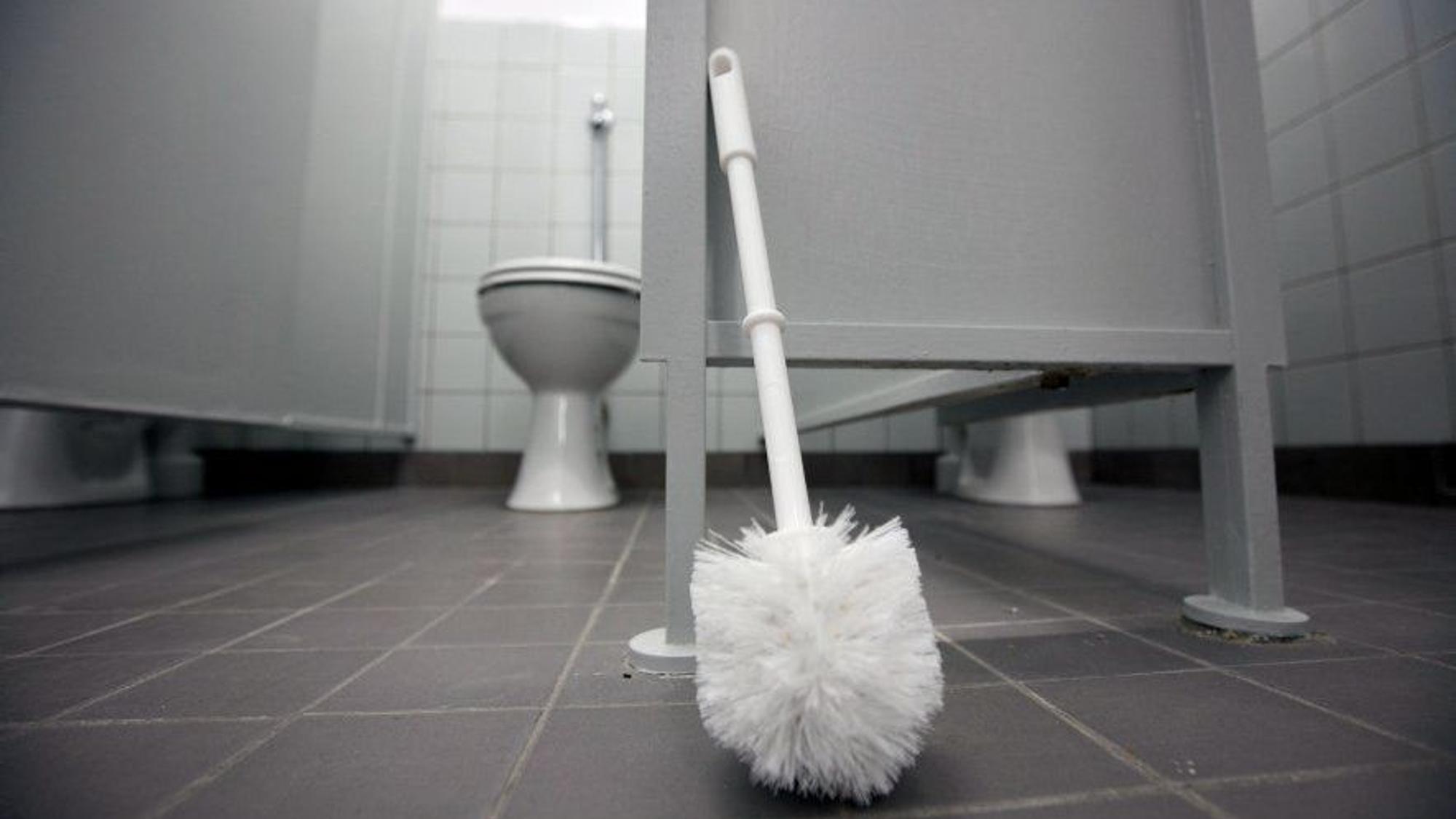 Eine Klobürste lehnt an einer Tür in Toilettentrakt.