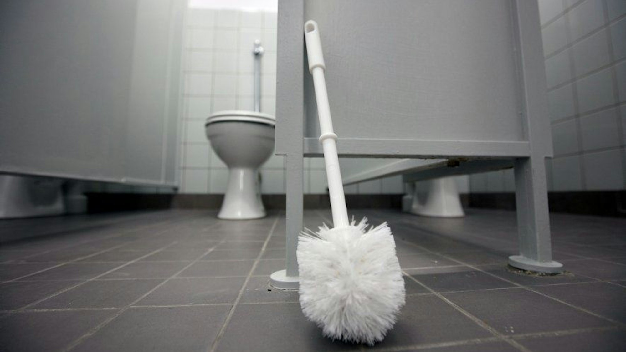 Eine Klobürste lehnt an einer Tür in Toilettentrakt.