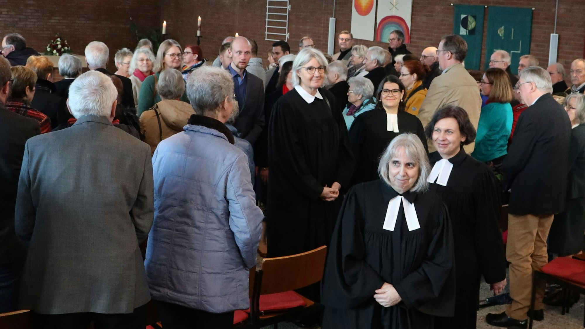 Pfarrerin Renate Kalteis und Gemeindesekretärin Elke Bell verlassen im Talar die Kirche. Die Menschen haben sich während des Gottesdienstes von ihren Plätzen erhoben.