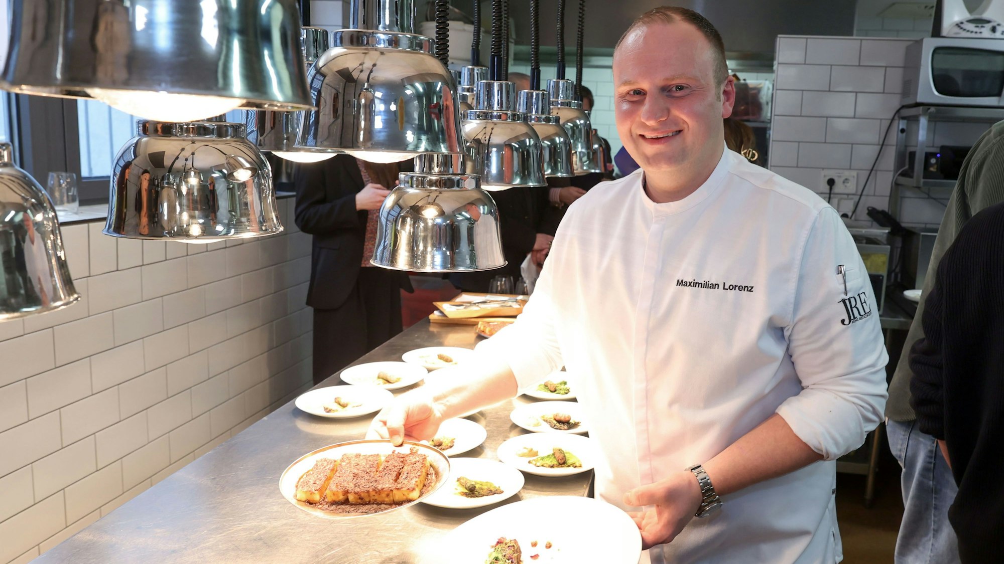 Koch Maximilian Lorenz hält in seiner Küche zwei Teller in die Kamera.