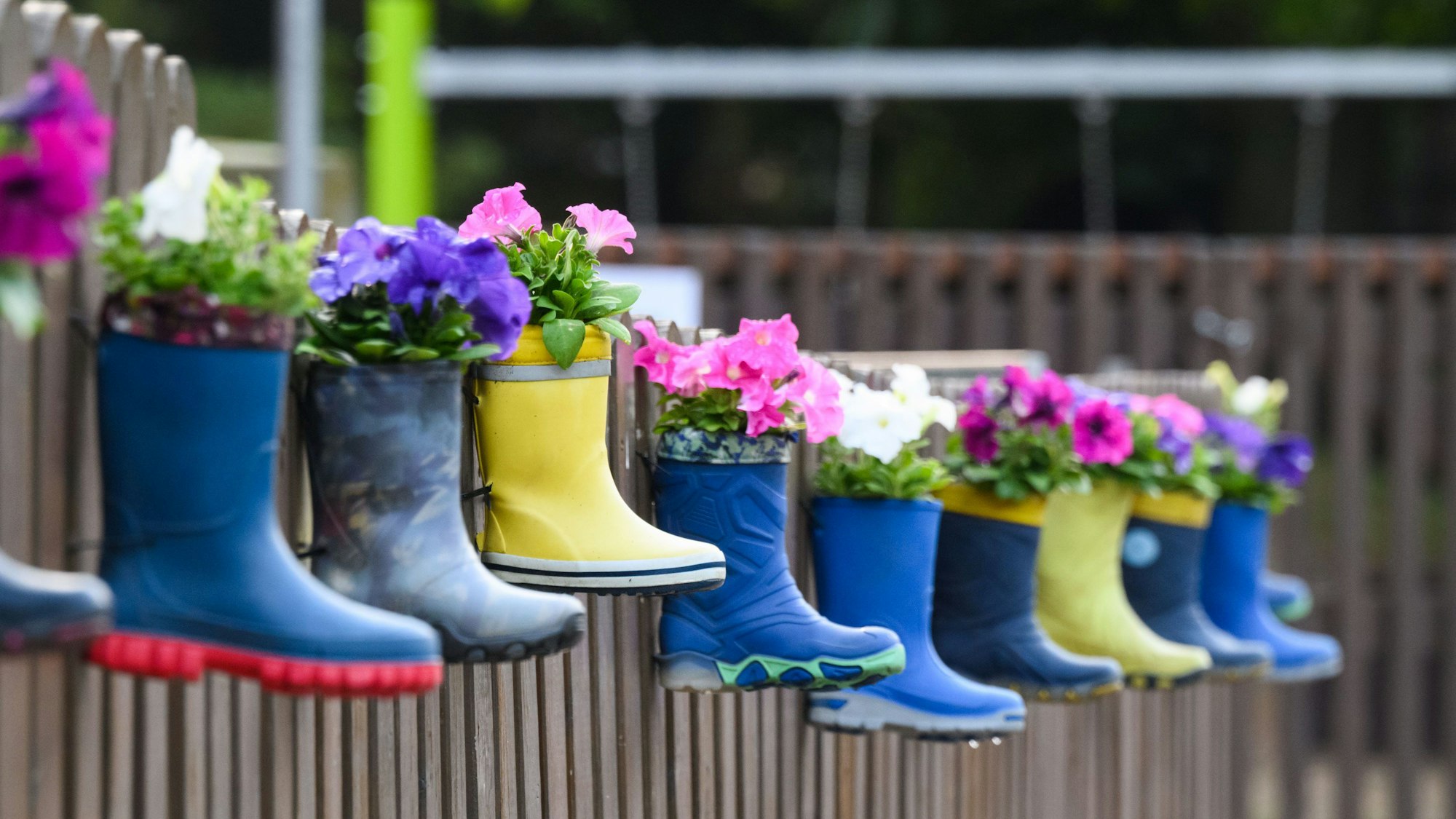 Gummistiefel von Kindern mit Blumen hängen am Zaun eines Kindergartens. (Symbolbild)