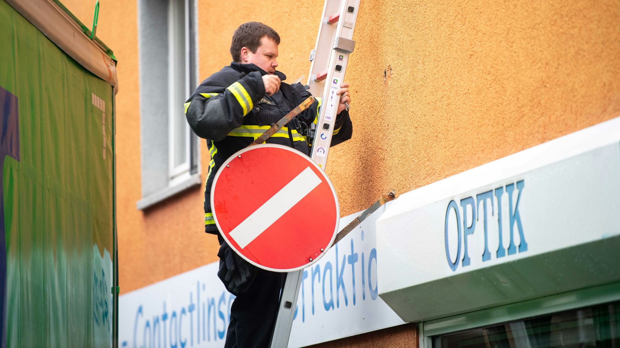 Das Bild zeigt einen Feuerwehrmann, der auf einer Leiter steht und ein Einbahnstraßenschild in der Hand hat.