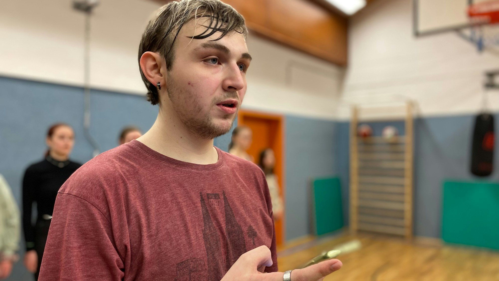 Mike Hilger steht in einer Turnhalle und sieht konzentriert aus. In seiner Hand hält er ein Smartphone, auf das er nicht schaut.