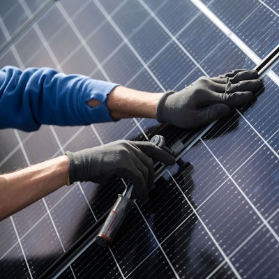 Ein Mann montiert Photovoltaikmodule auf dem Dach eines Wohnhauses.