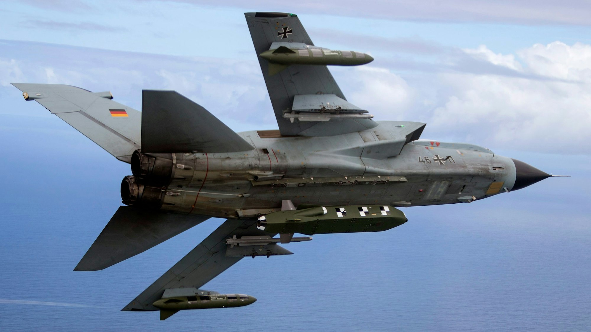 Ein Tornado-Kampfjet der Bundeswehr befindet sich im Flug über dem Meer. An seiner Unterseite ist ein Marschflugkörper des Typs Taurus angebracht. Unterhalb der Tragflächen sind weitere Raketen befestigt.