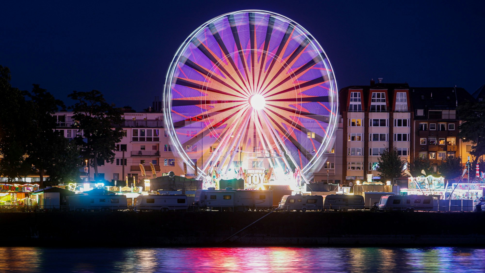 Das Europa-Riesenrad steht am Kölner Rheinufer und leuchtet lila im Dunkeln.