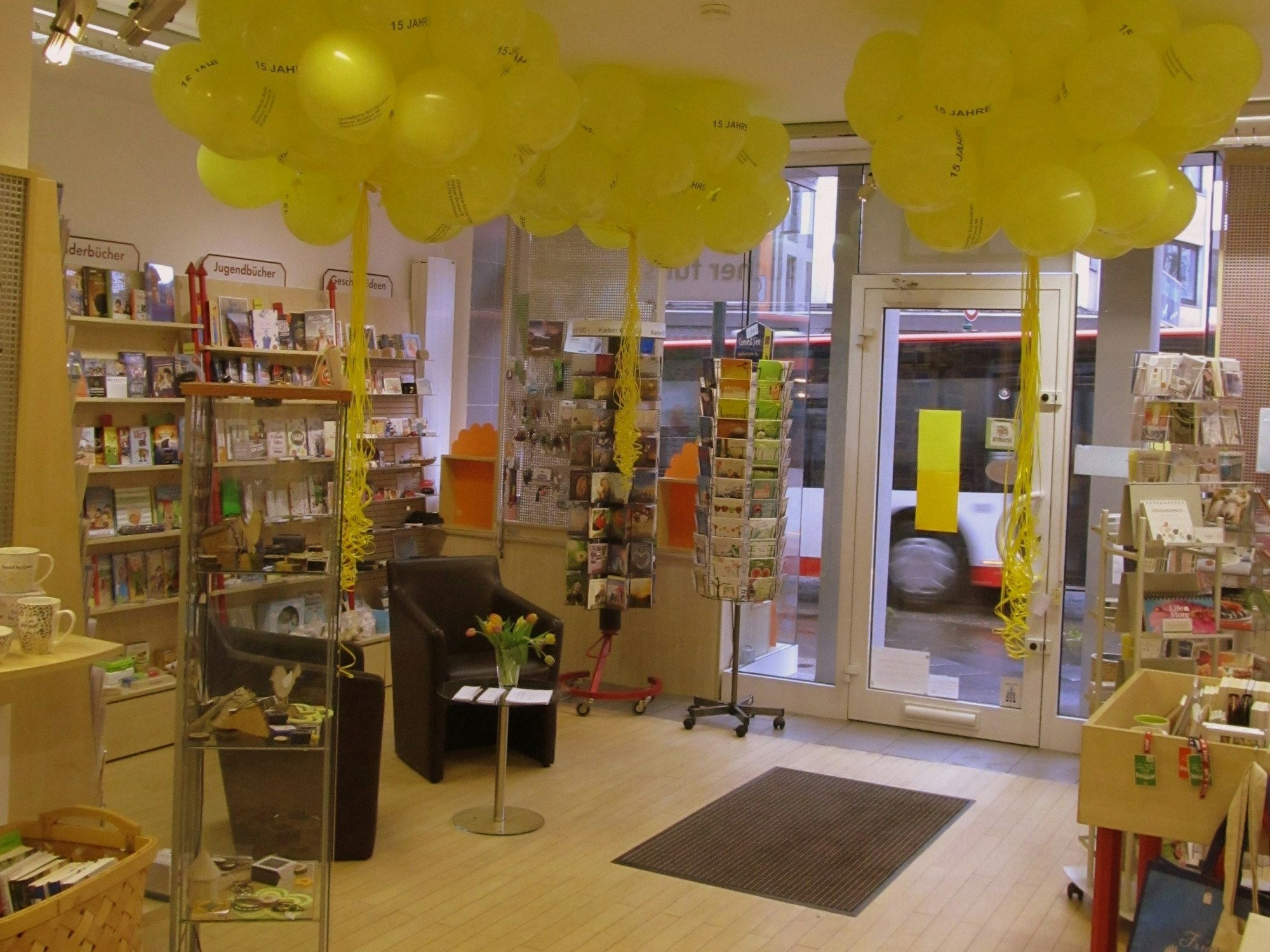 Der Buchladen von innen, zu sehen sind unter anderem mit Büchern gefüllte Regale, Kartenständer sowie zwei Sessel.