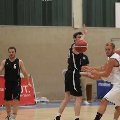 Im Basketball-Landesliga-Spiel gegen den TuS Brauweiler gerät Jan Philipp Thomas (Nr. 11) ins Straucheln. Vor ihm sein Mitspieler Christoph Gier. Der Ball ist weit weg, alle schauen ihm hinterher.