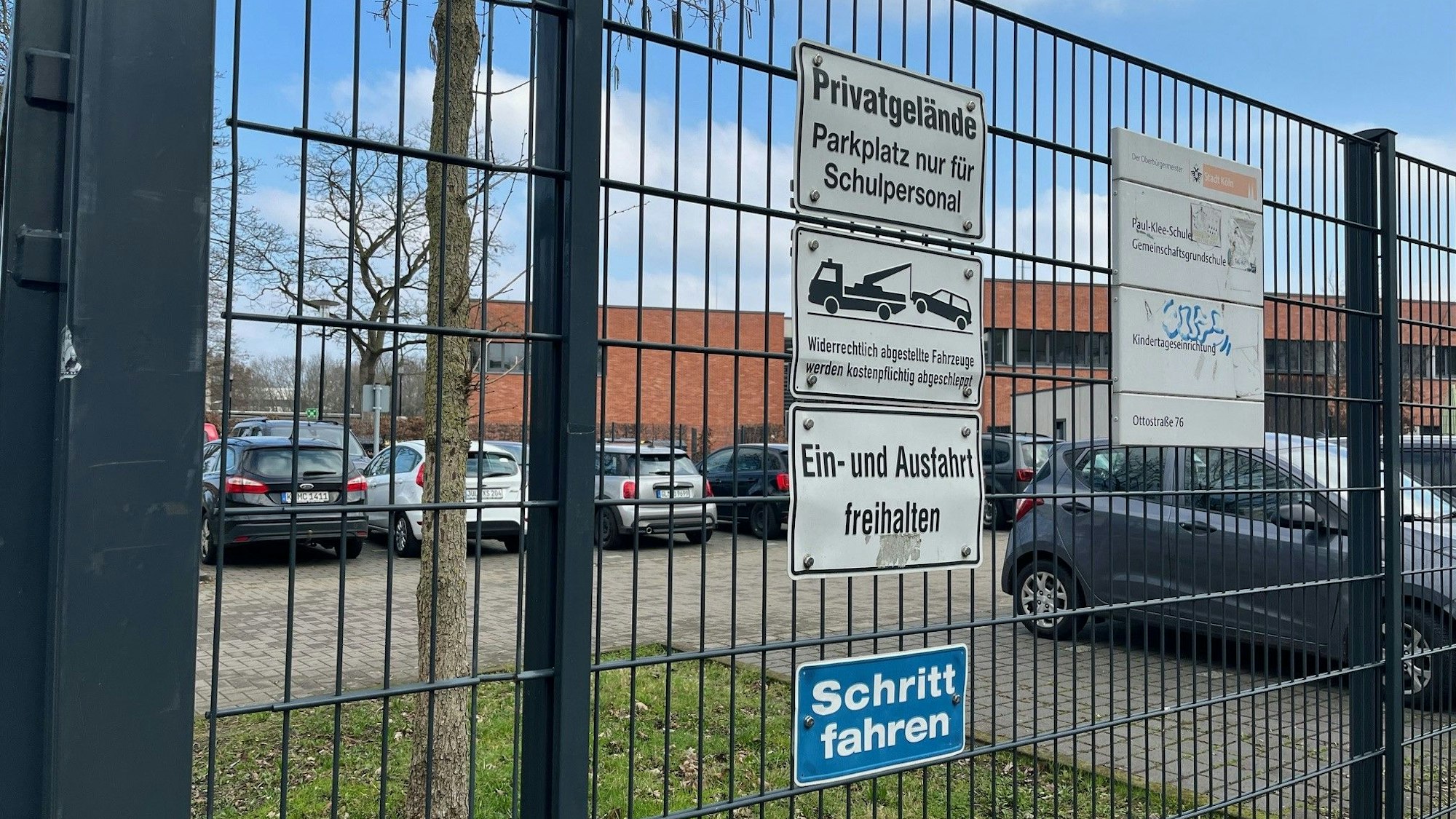 Ein Lehrerparkplatz mit Zaun davor.