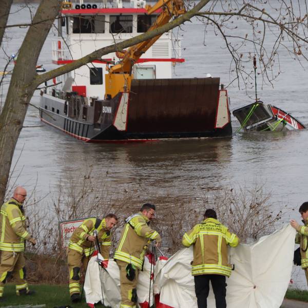 Das Bild zeigt Feuerwehrmänner am Ufer in Wesseling am Rhein.