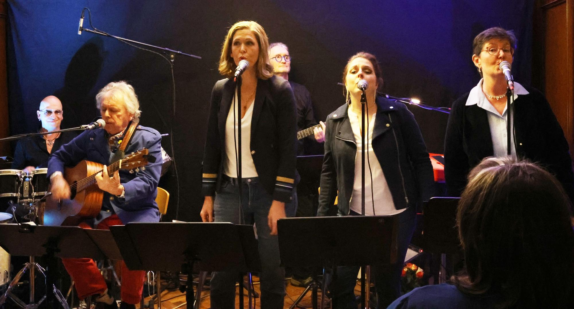 Die drei Sängerinnen stehen nebeneinander im Vordergrund, die Instrumentalisten sitzen dahinter.