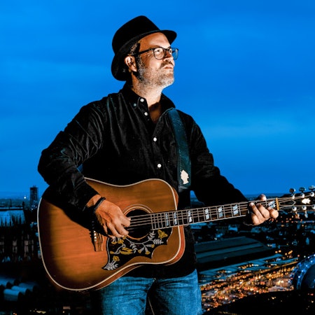 Björn Heuser steht mit Gitarre am Rheinufer