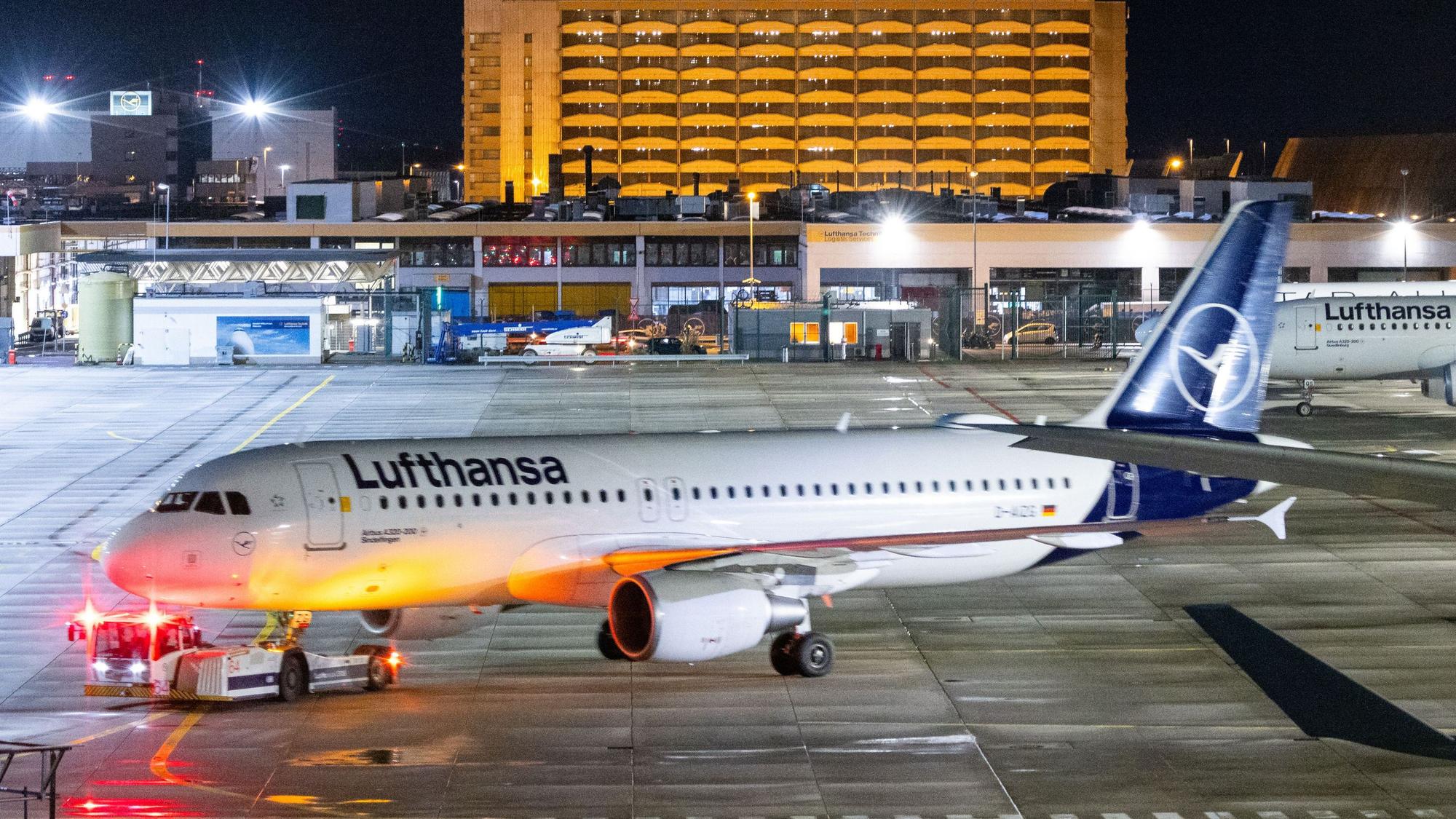 Ein Flugzeugschlepper zieht ein Flugzeug der Lufthansa auf einem Rollfeld. Mehrere Warnleuchten sind dabei angeschaltet. (Symbolbild)