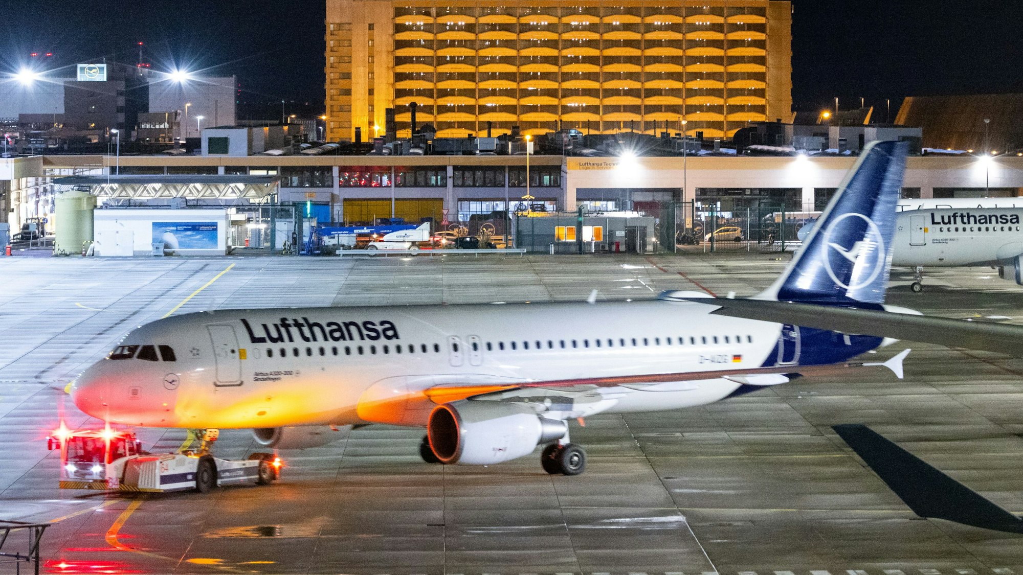 Ein Flugzeugschlepper zieht ein Flugzeug der Lufthansa auf einem Rollfeld. Mehrere Warnleuchten sind dabei angeschaltet. (Symbolbild)