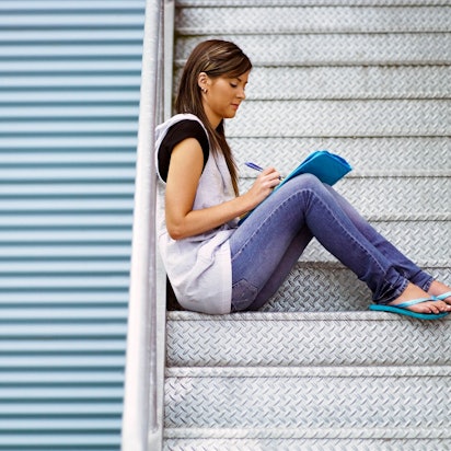 Frau sitzt auf Treppe und schreibt in ein Heft.