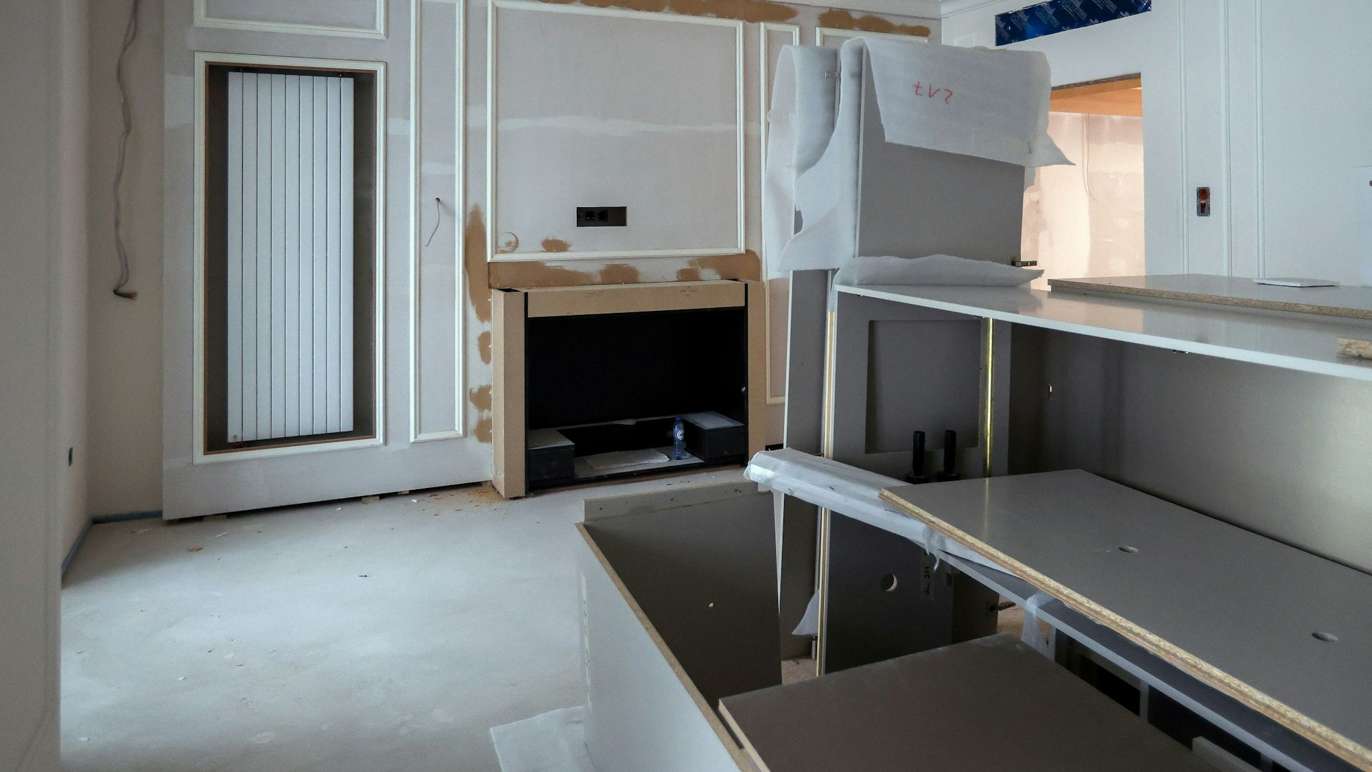 Das Bild zeigt ein Hotelzimmer, das sich noch im Bau befindet. Zu sehen sind eine Auslassung für den Kamin und eine Heizung sowie einige im Raum stehende Möbel.