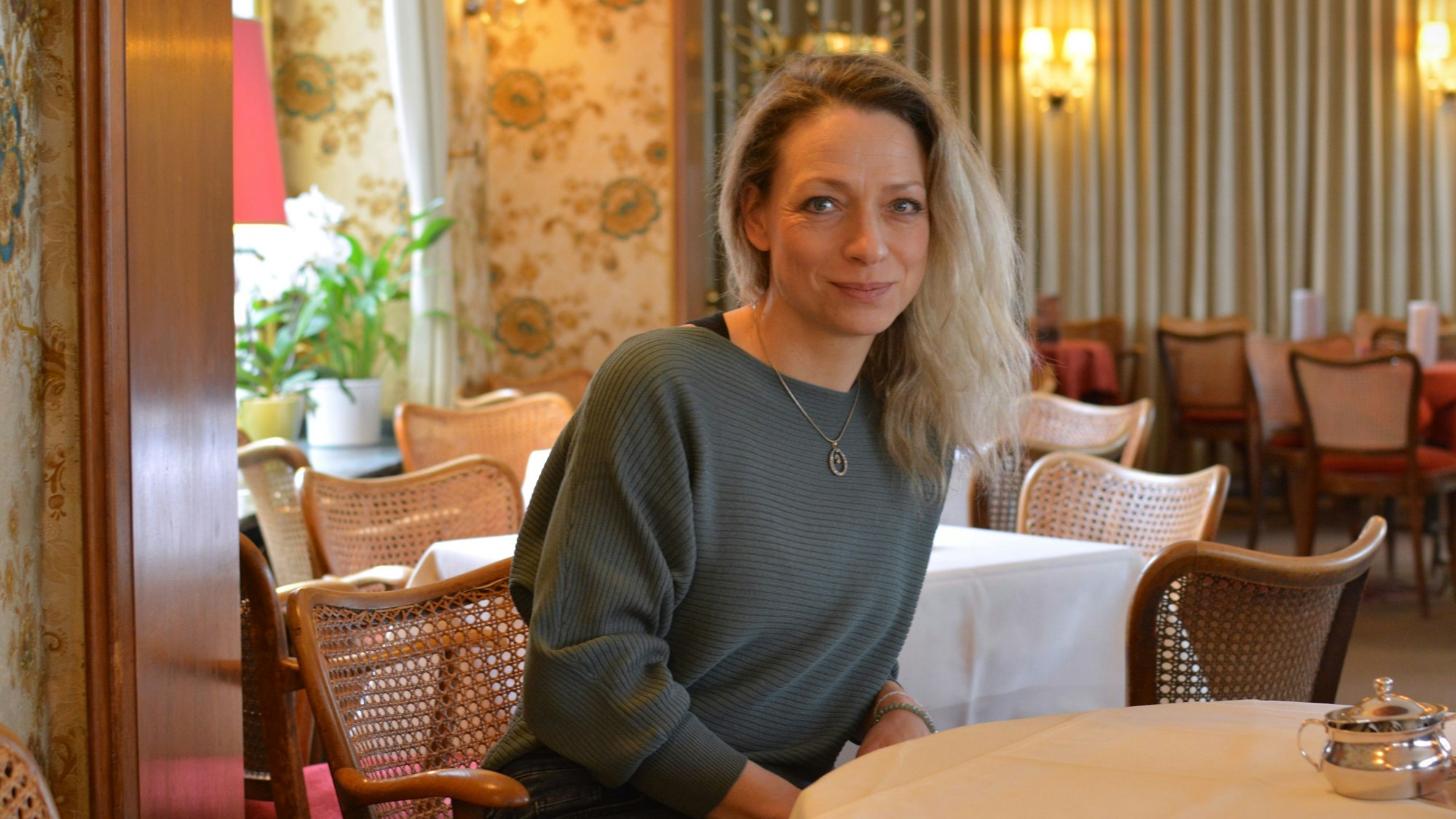 Carolin Soyka sitzt in einem Café, sie hat mittellange blonde Haare und trägt einen blaugrauen Pullover.