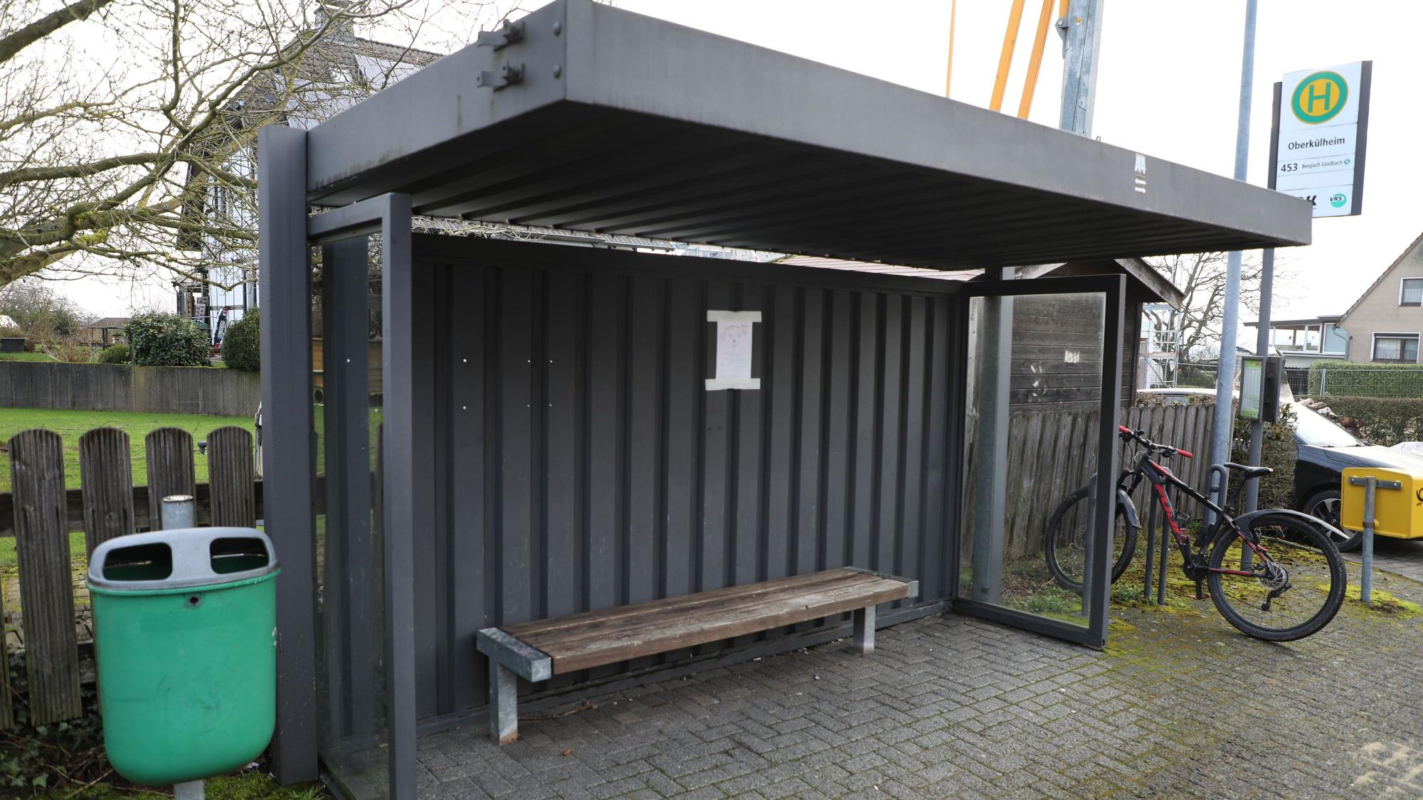 Die Bushaltestelle „Oberkühlheim“ in Bergisch Gladbach mitsamt Mülleimer links, Fahrradständer und Briefkasten rechts. Die Haltestelle bietet eine Sitzbank und einen Fahrplan.