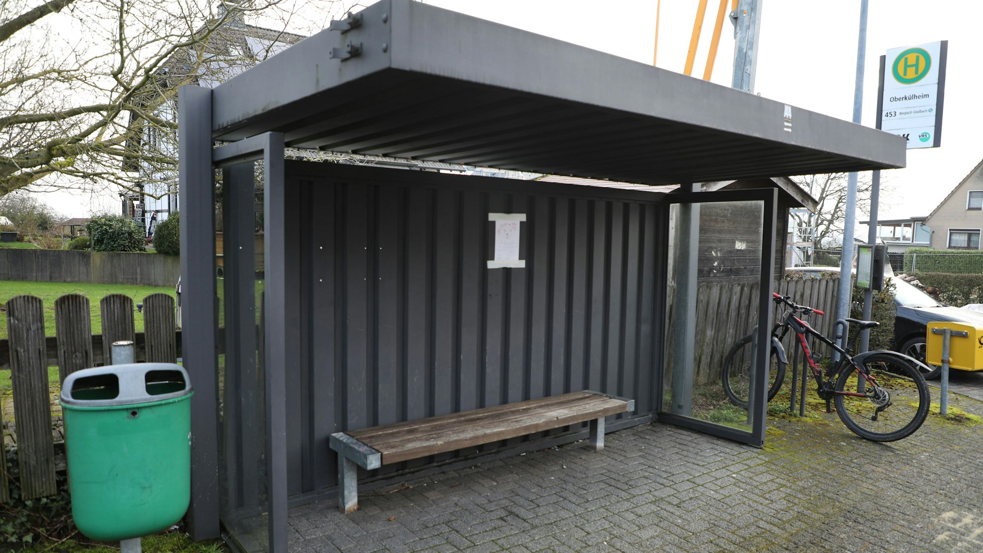 Die Bushaltestelle „Oberkühlheim“ in Bergisch Gladbach mitsamt Mülleimer links, Fahrradständer und Briefkasten rechts. Die Haltestelle bietet eine Sitzbank und einen Fahrplan.
