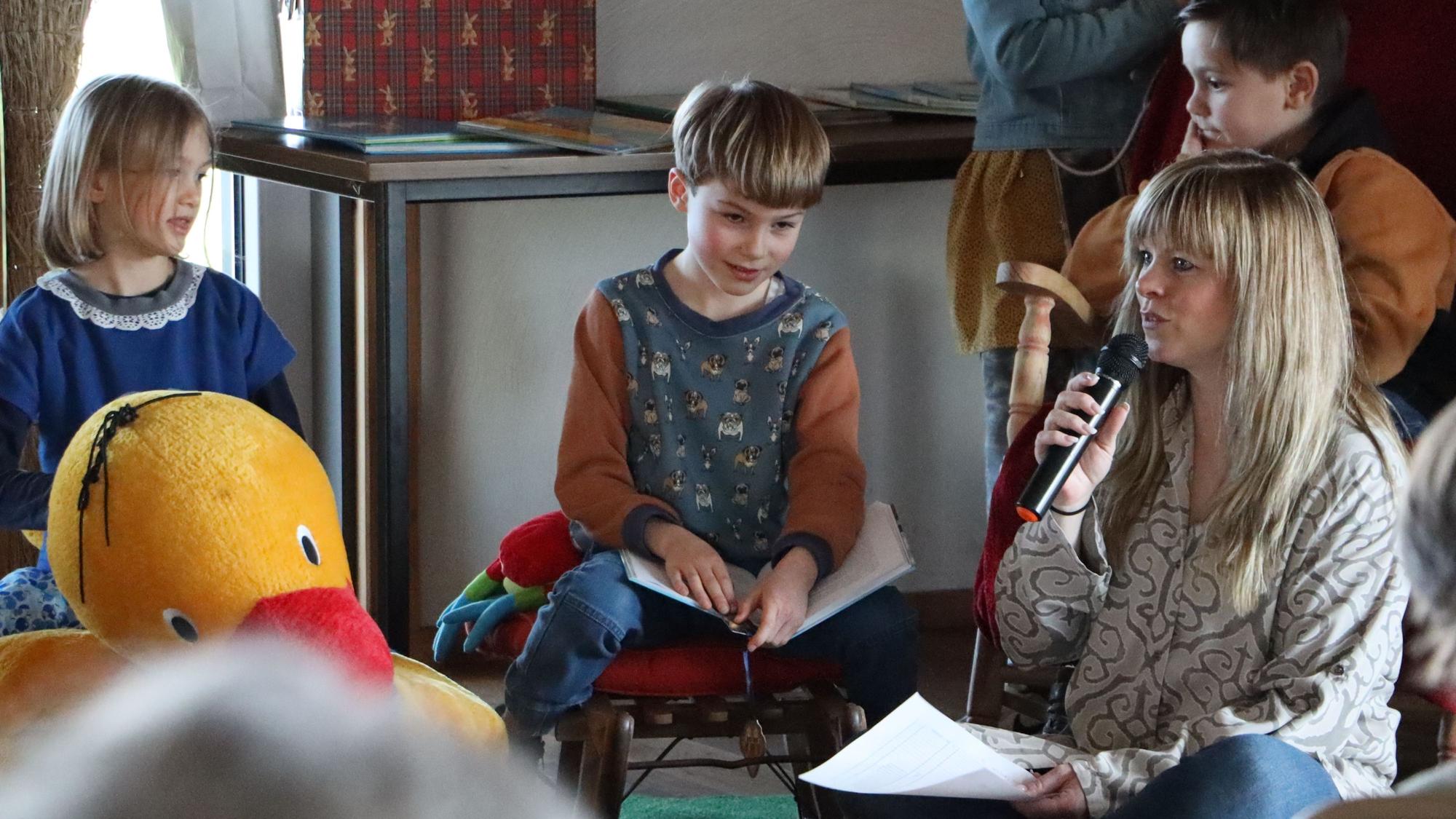 Danica Lorbach moderiert mit Mikrofon in der Hand. Zwei Kinder hören zu.