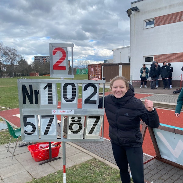 Victoria Krause steht neben der Anzeigentafel, auf der die Siegesweite von 57,87 Meter abgebildet ist und ballt ihre Faust.