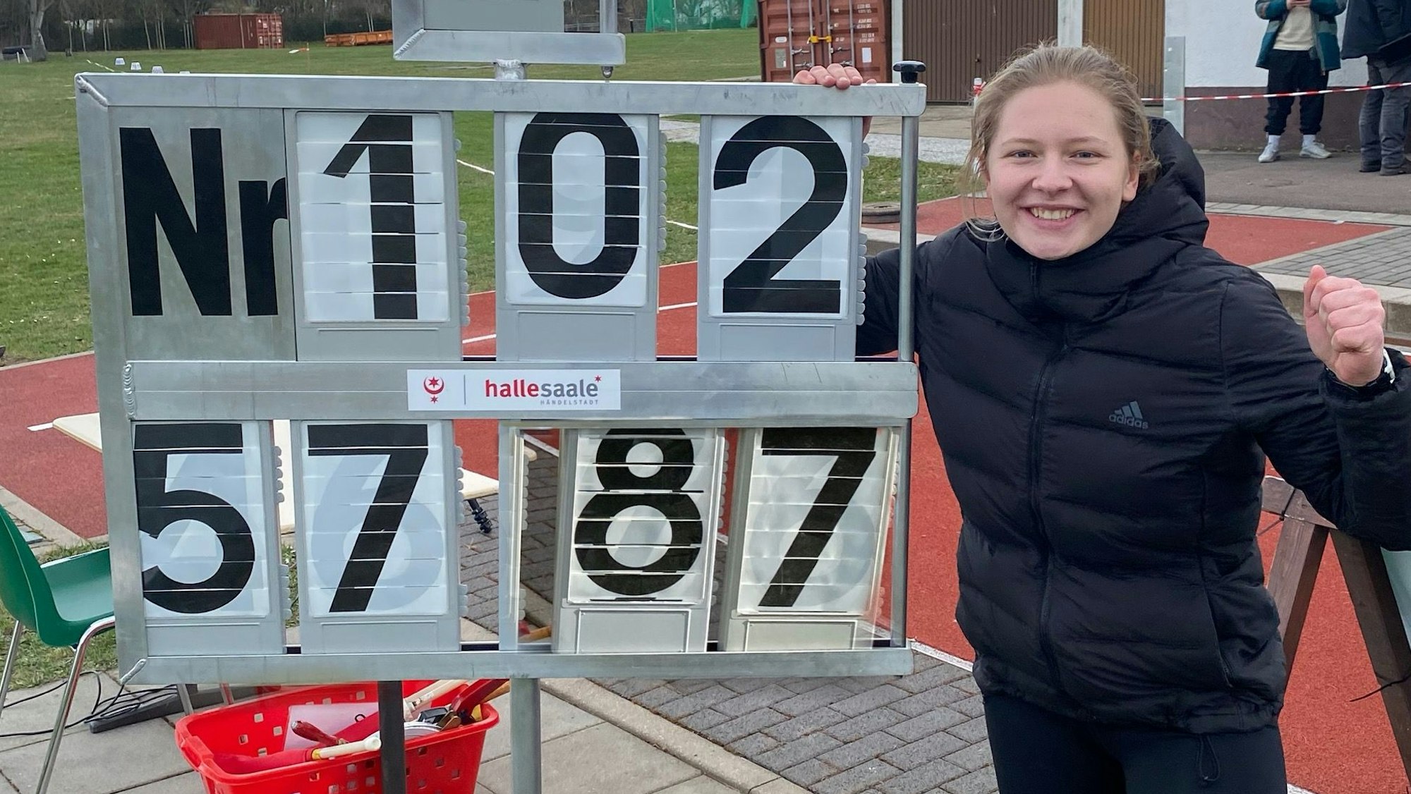 Victoria Krause steht neben der Anzeigentafel, auf der die Siegesweite von 57,87 Meter abgebildet ist und ballt ihre Faust.