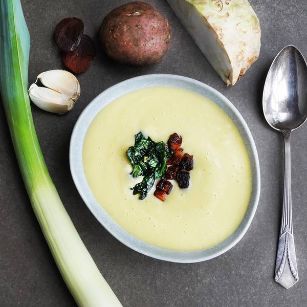 Die Suppe ist mit Spinat verziert in einem Suppenteller angerichtet. Daneben liegt ein Löffel und Gemüse.