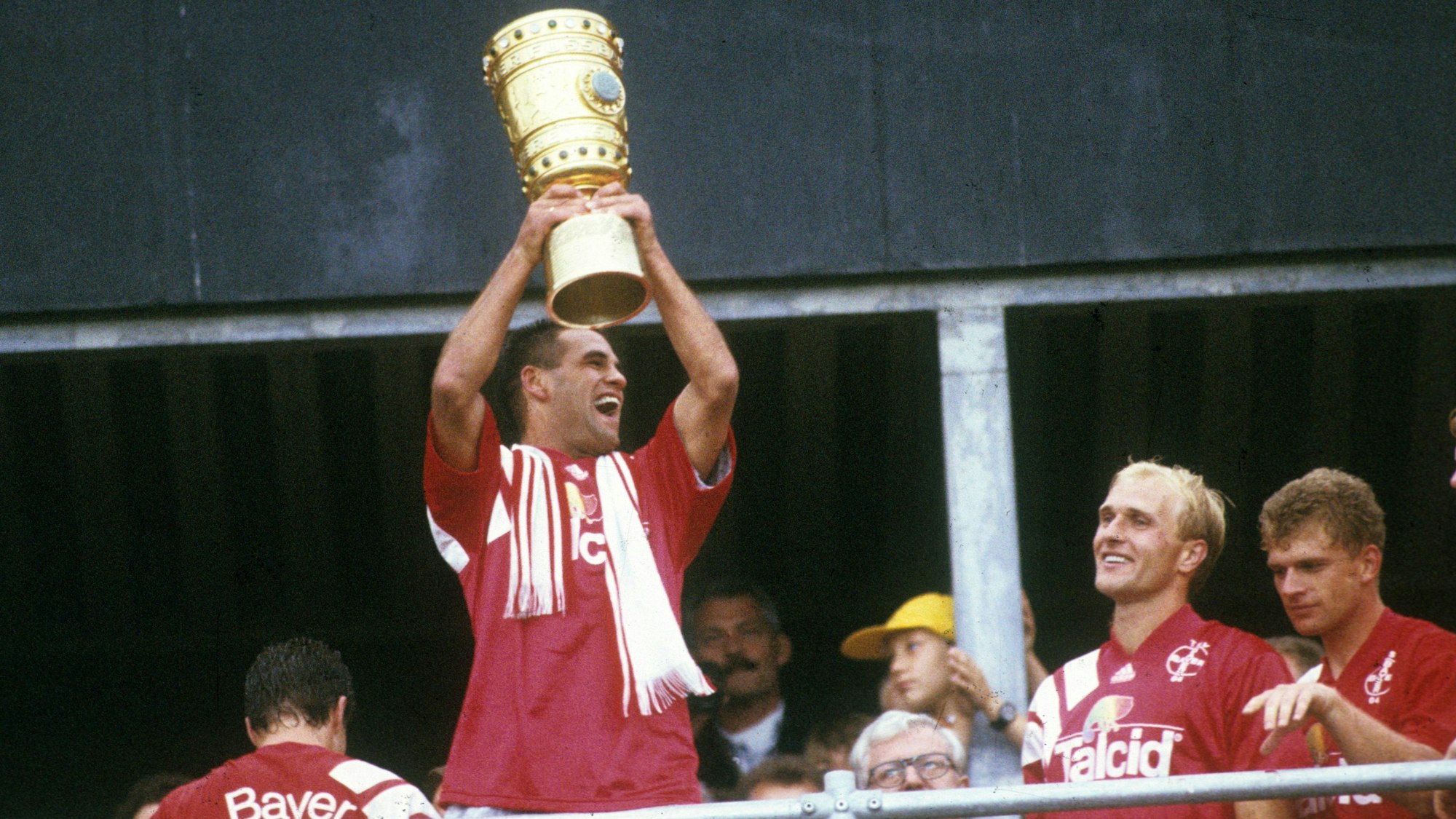 Spieler von Bayer Leverkusen stehen an einer Brüstung und halten jubelnd den DFB-Pokal in die Höhe.