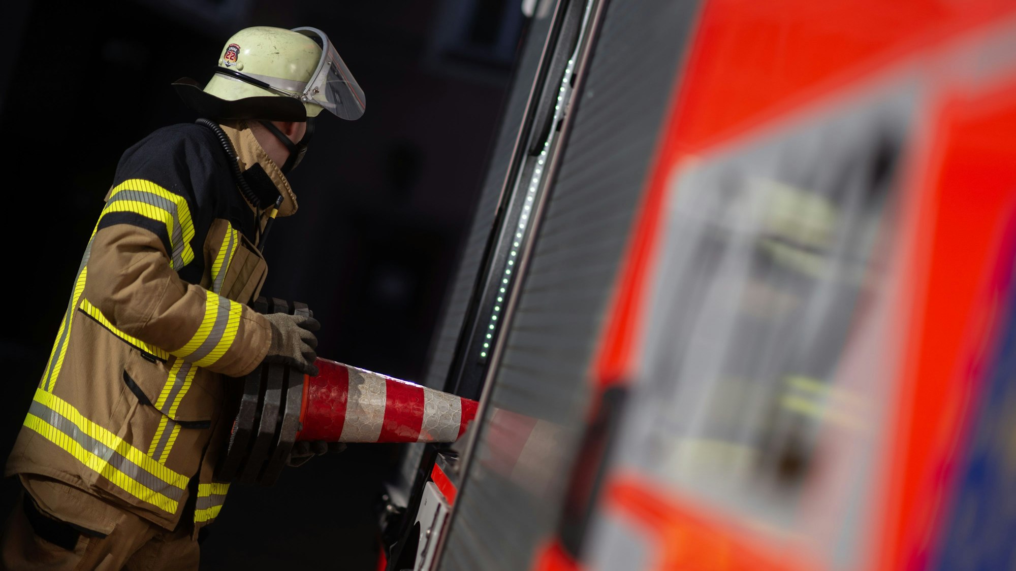 Eine Einsatzkraft der Feuerwehr nimmt eine Pylone aus einem Einsatzfahrzeug der Feuerwehr