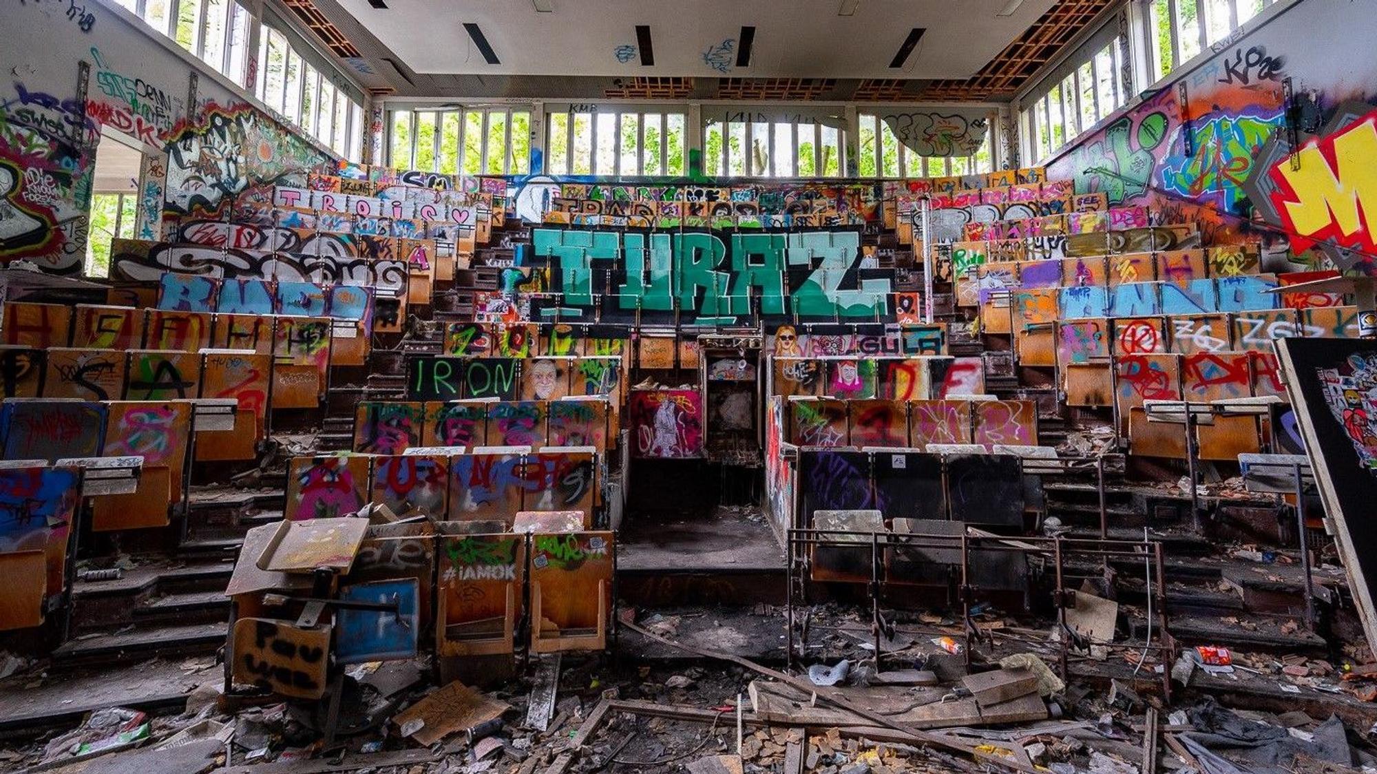 Zu sehen ist ein heruntergekommener und mit Grafitti besprühter Hörsaal.