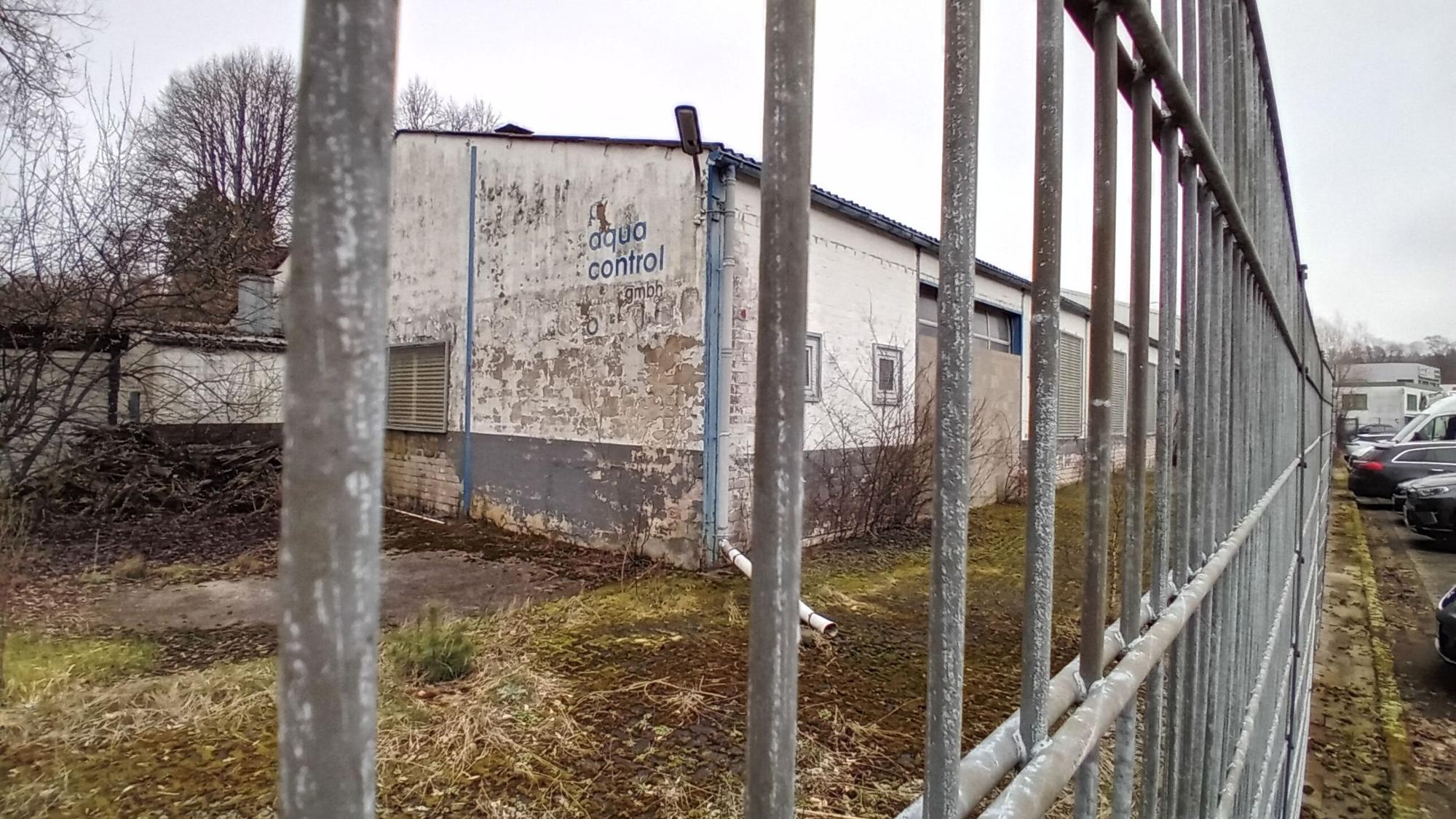 Ein heruntergekommenes Industriegebäude hinter einem Zaun mit der Aufschrift „Aqua Control“.
