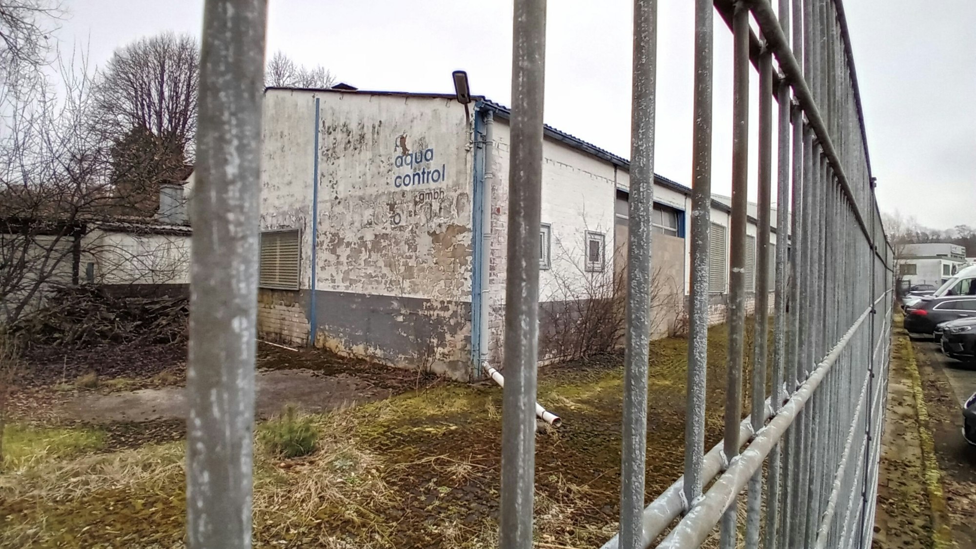 Ein heruntergekommenes Industriegebäude hinter einem Zaun mit der Aufschrift „Aqua Control“.