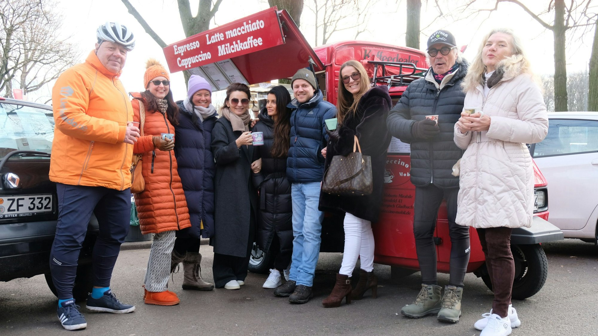Eine Gruppe Menschen stehen im Halbkreis vor einem feuerroten Kaffeemobil.