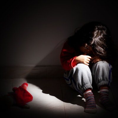 Ein kleines Mädchen sitzt zusammengekauert in einem dunklen Raum.