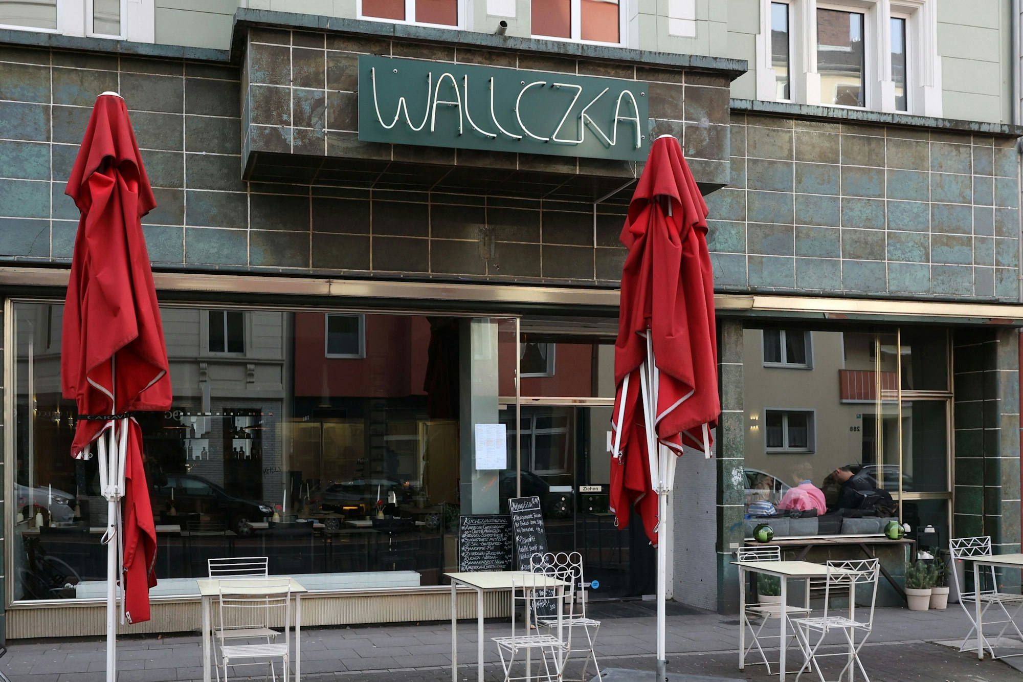 Das Restaurant Wallczka in Ehrenfeld mit Plätzen draußen und roten Sonnenschirmen.