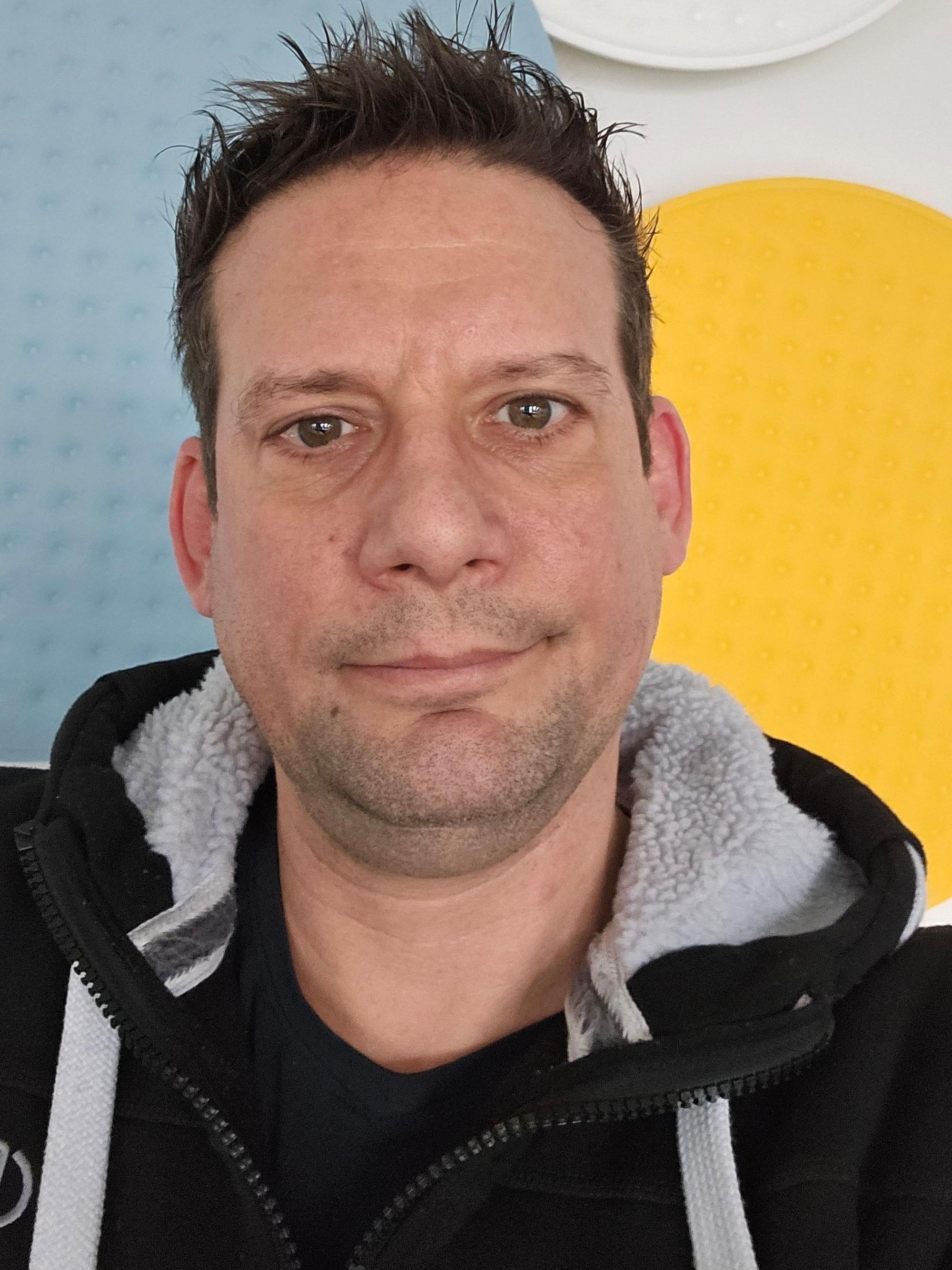 Ein dunkelhaariger Mann in einem Sweatshirt.