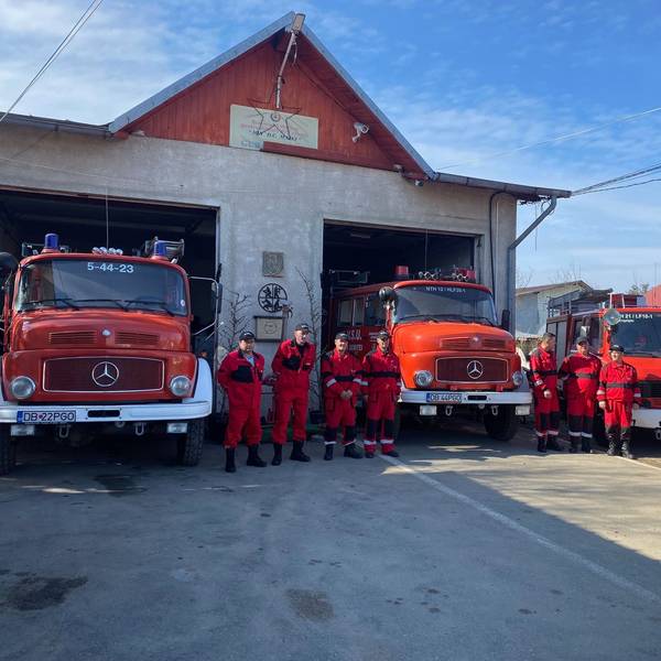 Rot gekleidete Feuerwehrleute stehen vor drei roten Feuerwehrwagen.