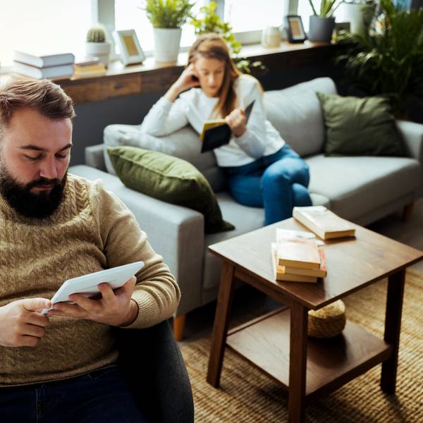 Paar sitzt im Wohnzimmer, beide lesen für sich.