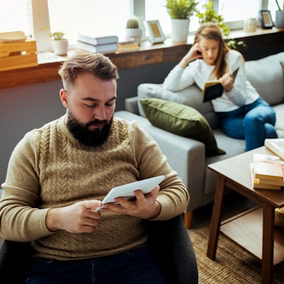 Paar sitzt im Wohnzimmer, beide lesen für sich.
