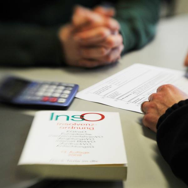 Ein Mann sitzt in einem Beratungsgespräch bei der Schuldner- und Insolvenzberatungsstelle. Ein Mitarbeiter füllt das Formular aus, im Vordergrund liegt ein Buch über die Insolvenzordnung.