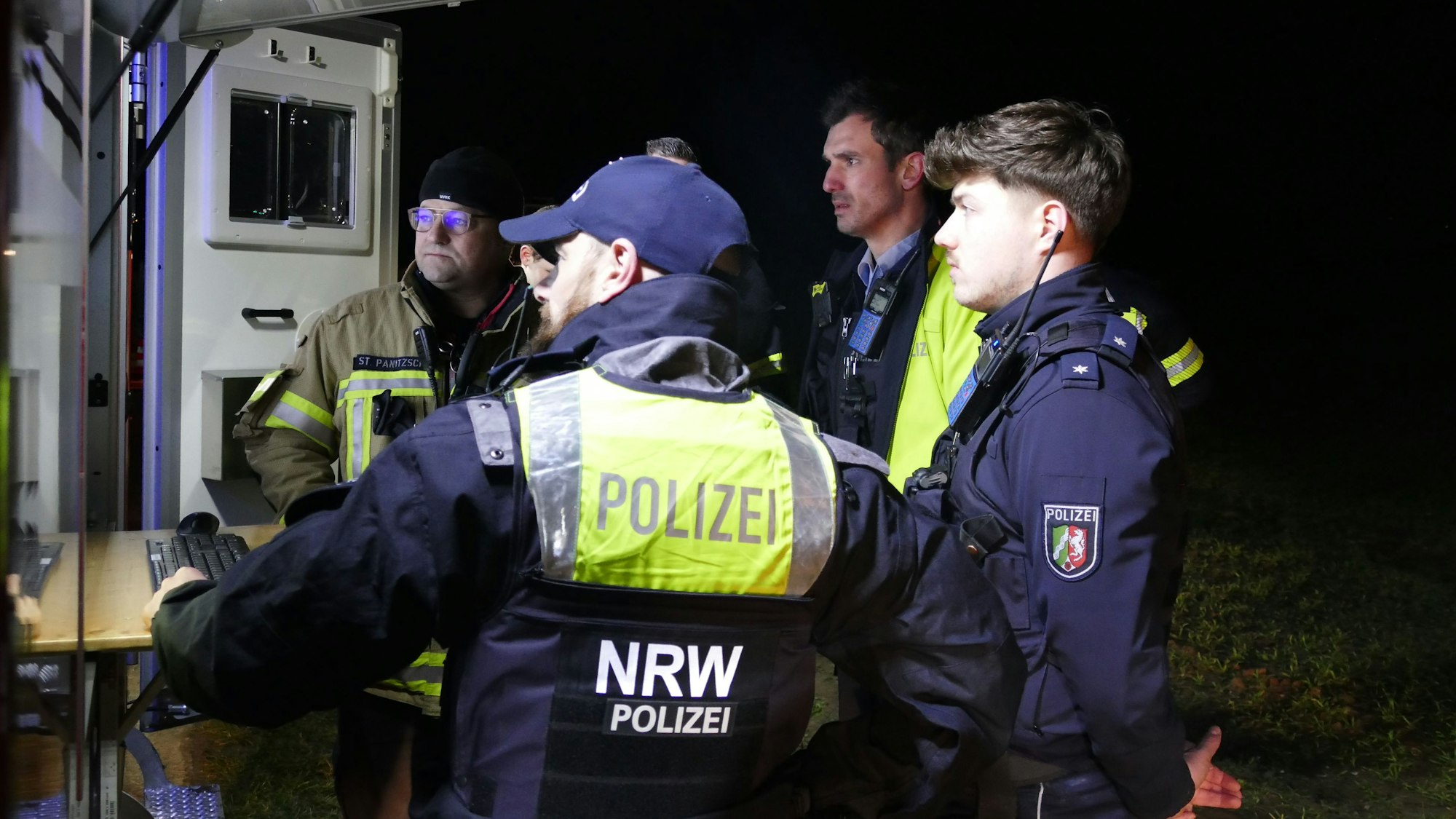 Polizisten und Feuerwehrleute schauen auf den Bildschirm, der das Bild der Wärmebildkamera anzeigt.