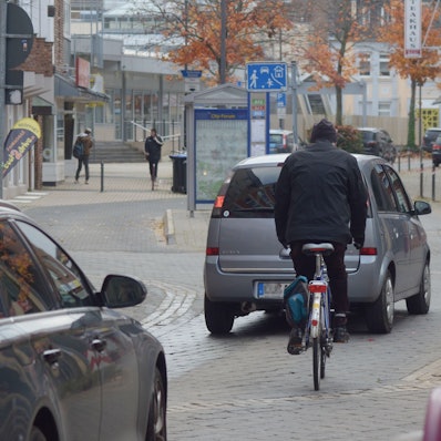 Das Bild zeigt einen Radfahrer in der Euskirchener Innenstadt. Vor und hinter ihm fahren Autos.