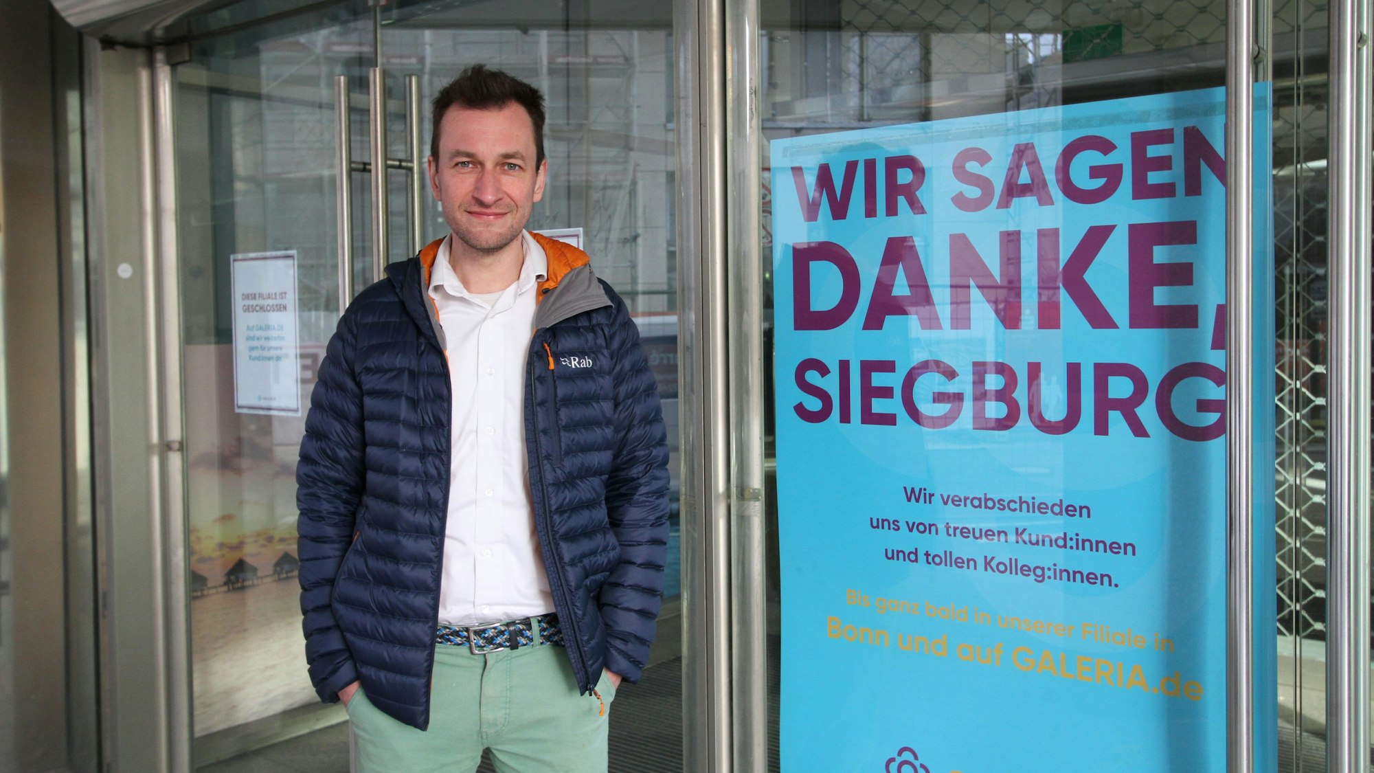 Ein Mann in einem blauen Blouson vor der geschlossenen Tür eines Warenhauses