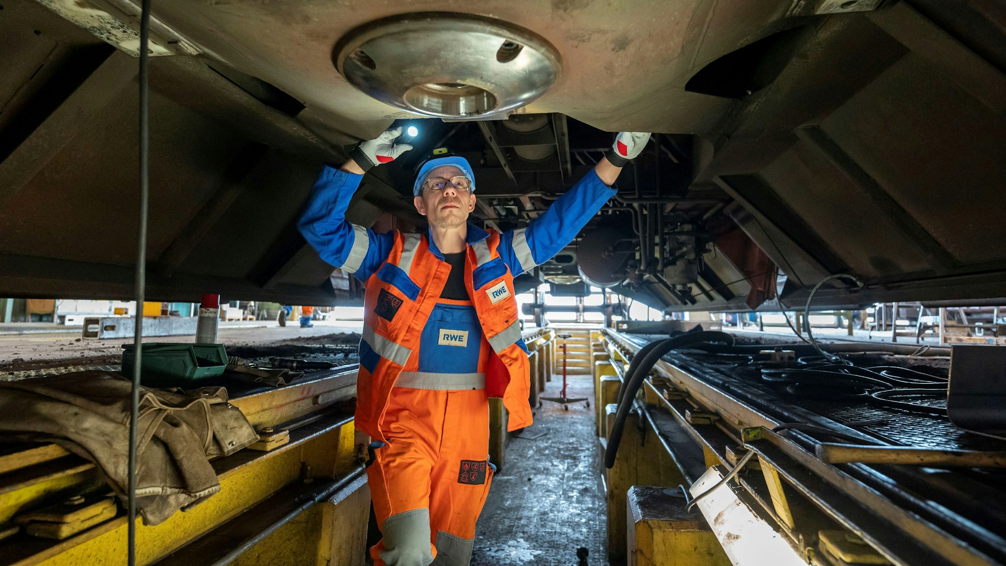 Auf dem Bild ist ein Arbeiter zu sehen, der einen Zug von unten repariert