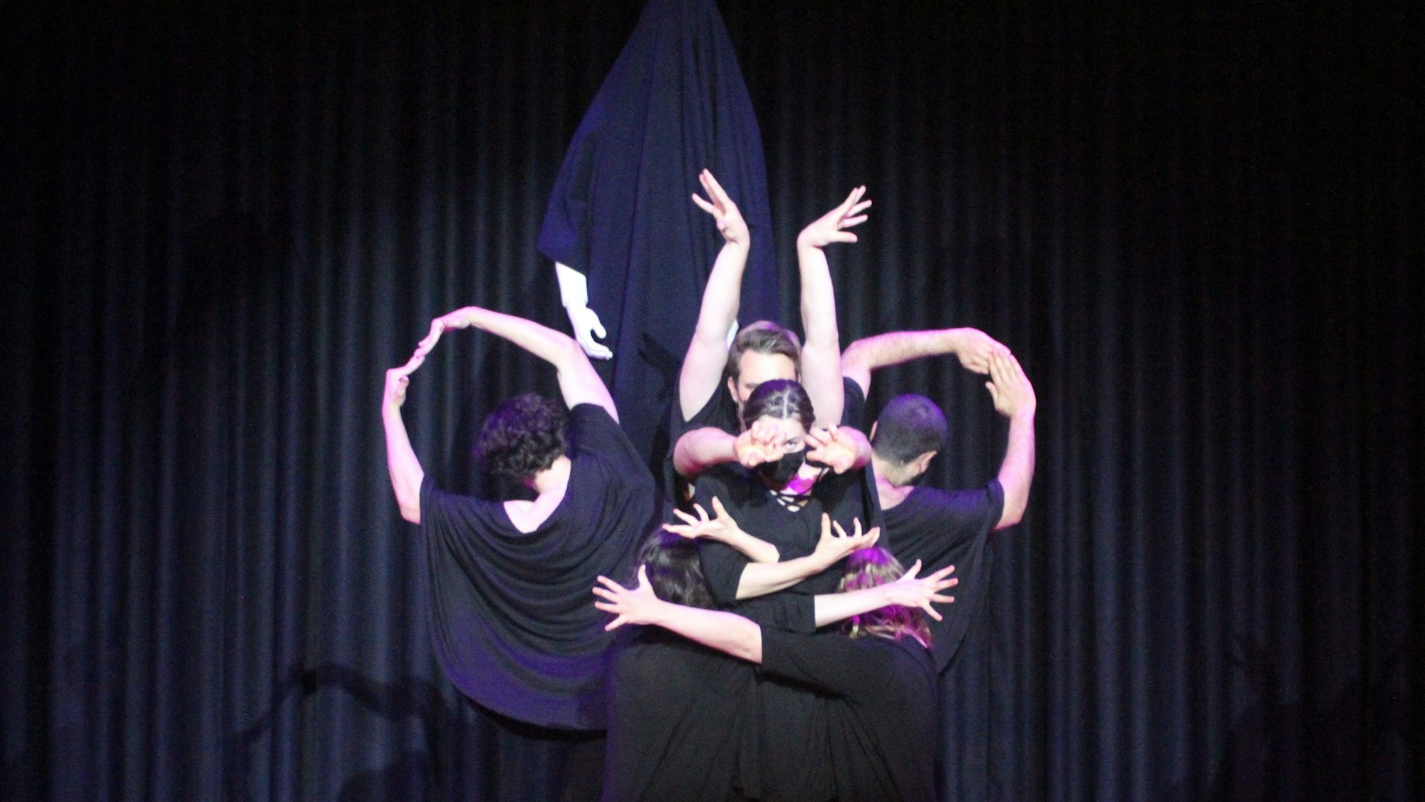 Schwarz kostümierte Schauspieler in einer Tanzfigur auf einer dunklen Bühne