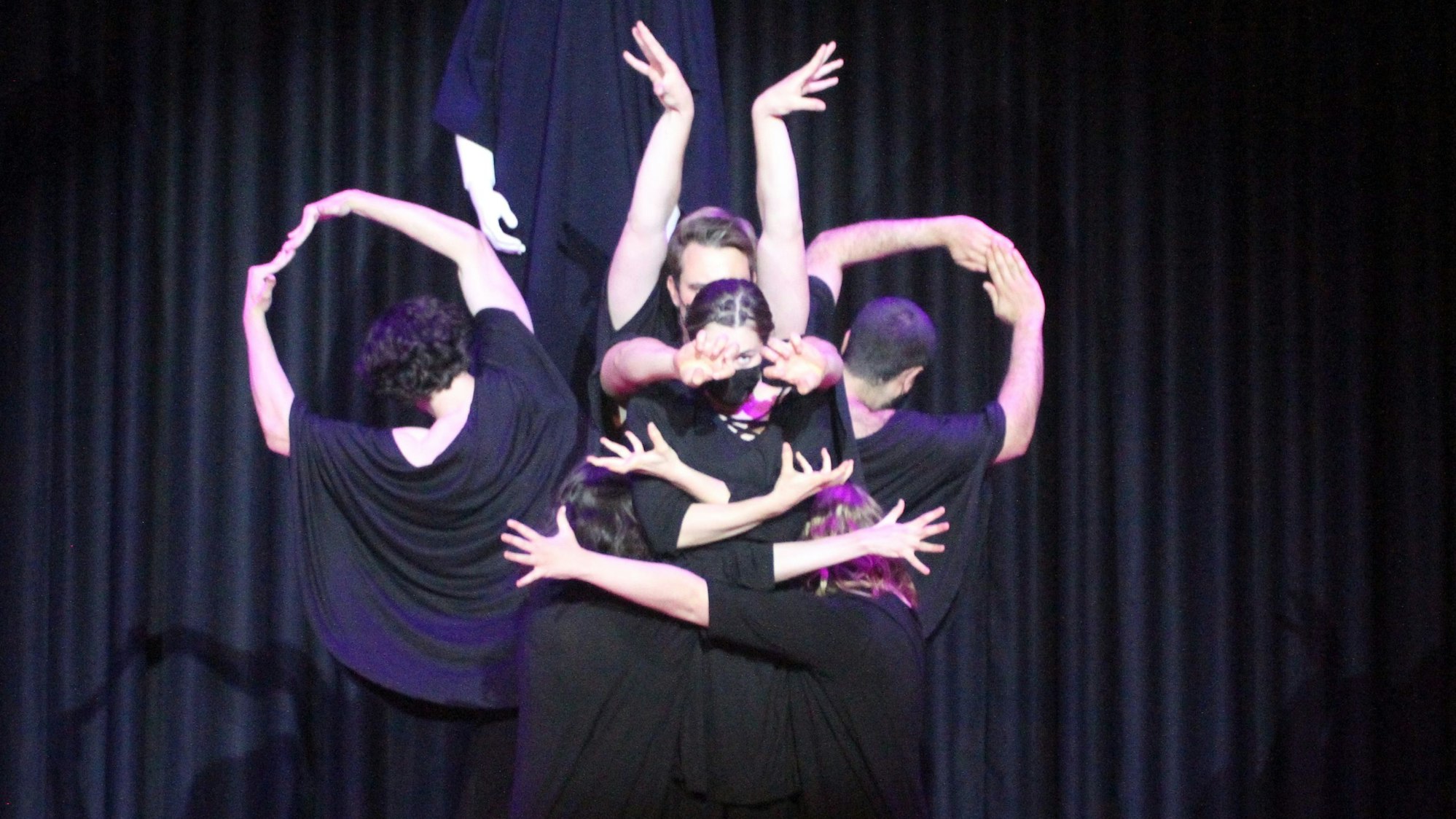 Sechs schwarz gewandete Schauspieler umschlingen sich auf einer Bühne.