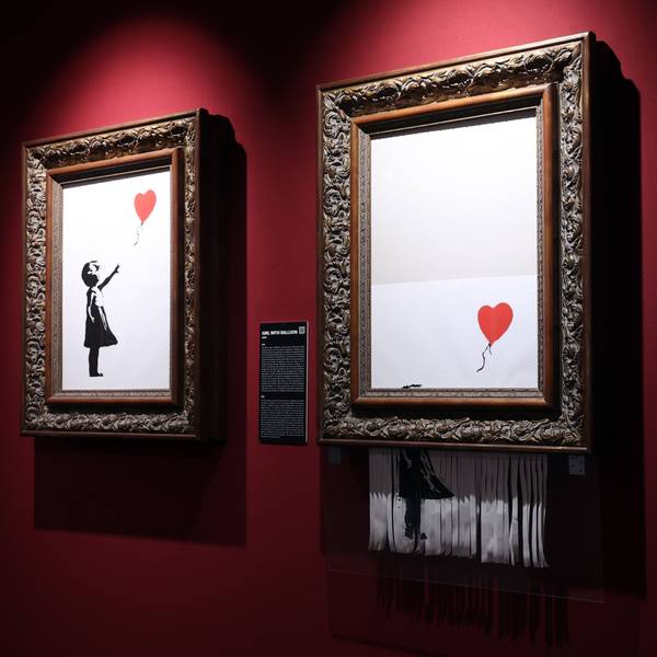Zwei Bilder von Banksy hängen an einer roten Wand.